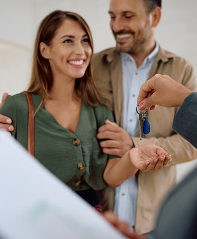 Happy woman and her husband getting keys from real estate agent while buying a new apartment.