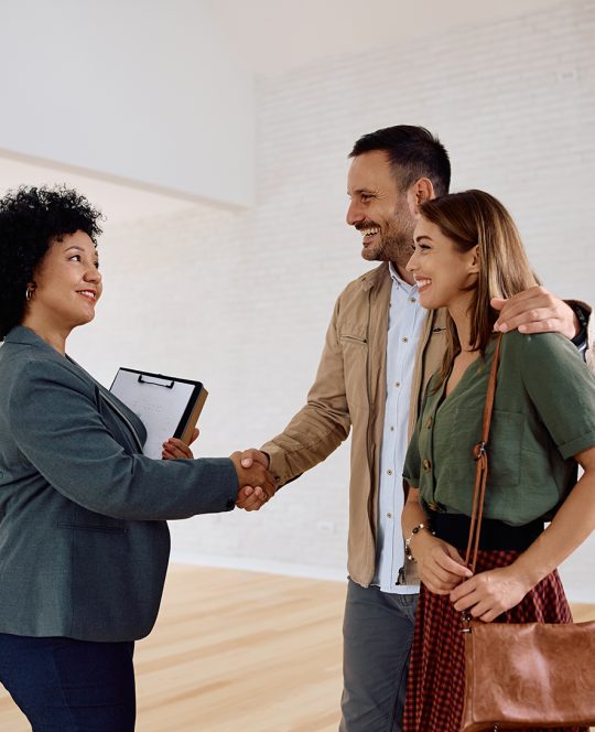 Happy real estate agent greeting a couple during open house day.